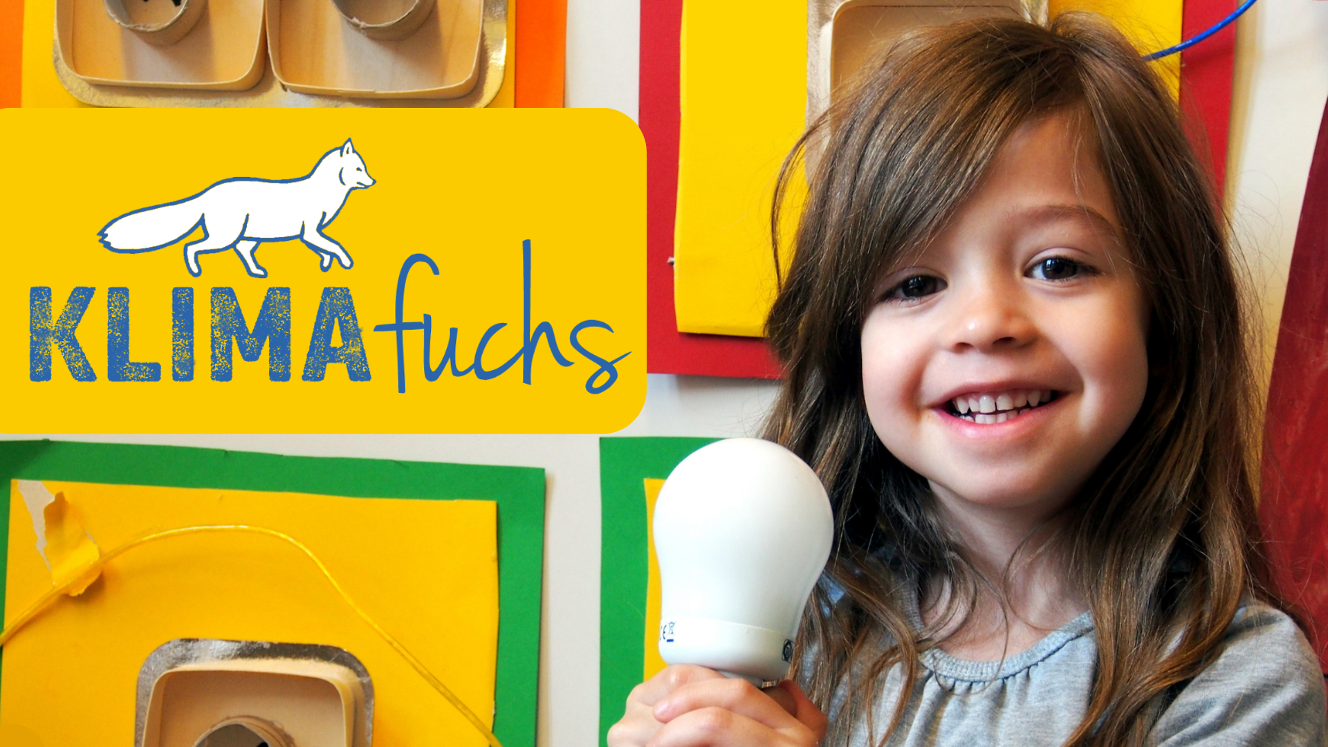 Ein kleines Mädchen hält eine Energiesparlampe in beiden Händen und lächelt in die Kamera.